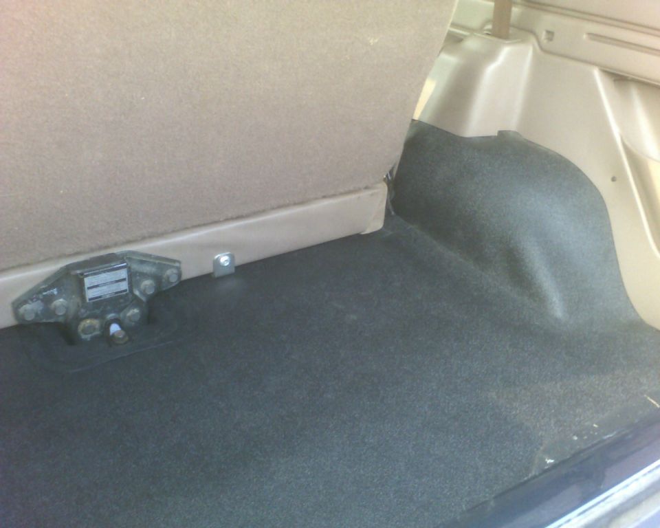 Trunk interior of a sedan showing carpet and a tow component
