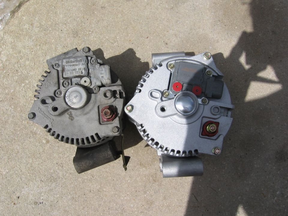 Two Ford alternators, one older and one newer, sit on a concrete surface
