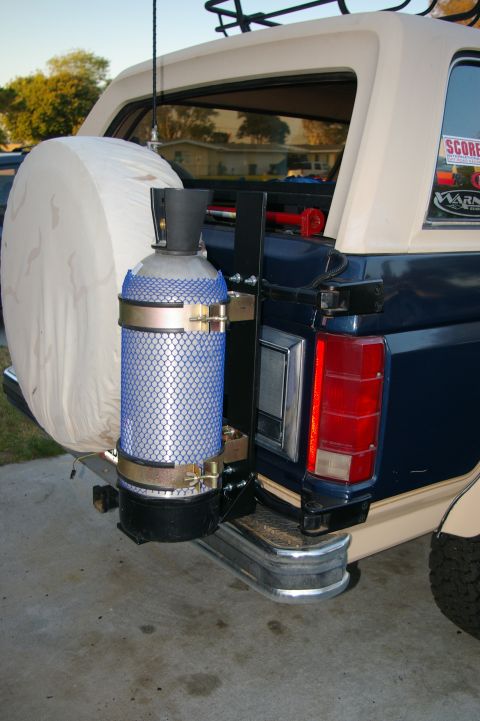 1986 Ford Bronco - The rear of a blue Ford Bronco shows a spare tire carrier and an external fuel tank mounted on the bumper.