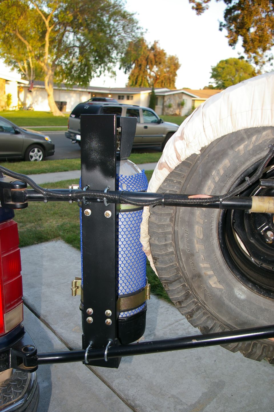 Spare tire carrier mounted on a vehicle's rear, holding a propane tank