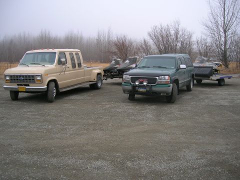 2003 Jeep TJ - Two vehicles, a Ford van and a GMC pickup, are parked and towing snowmobiles on a trailer.