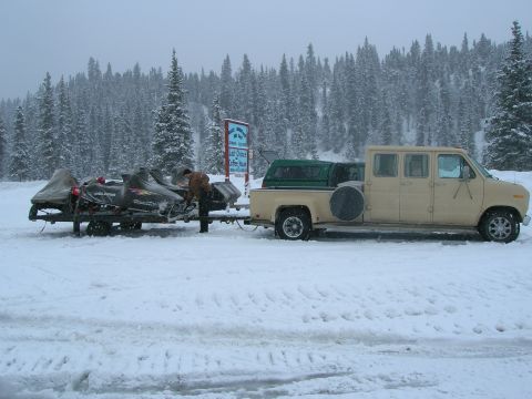 2003 Jeep TJ - A van tows snowmobiles on a trailer through a snowy landscape with a forest in the background.
