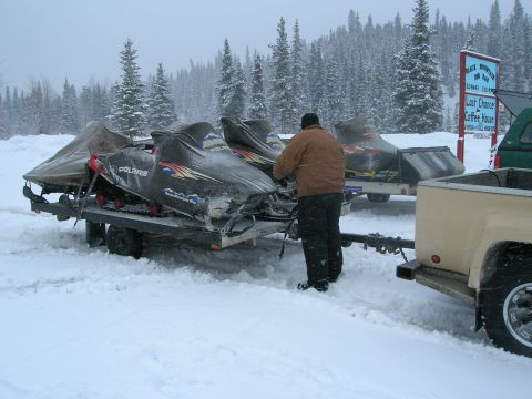 2003 Jeep TJ - A person loads snowmobiles onto a trailer in a snowy environment, with a sign for a local inn and coffee house visible.
