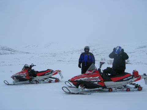 2003 Jeep TJ - Two individuals stand with their snowmobiles in a snowy, overcast landscape.