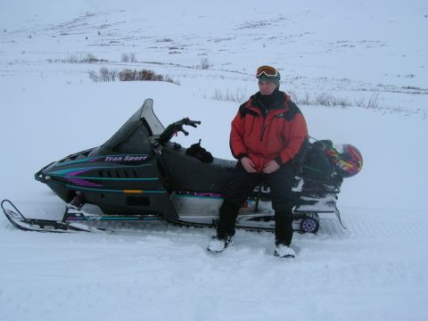 2003 Jeep TJ - A person is seated on a snowmobile in a snow-covered area with hills in the background.