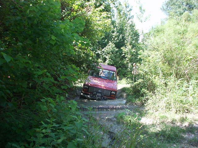 Red van stuck in a muddy ditch surrounded by trees