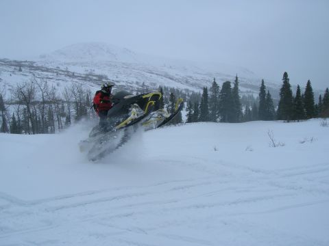 2003 Jeep TJ - Snowmobile rider navigates a snow-covered landscape with trees and mountains.