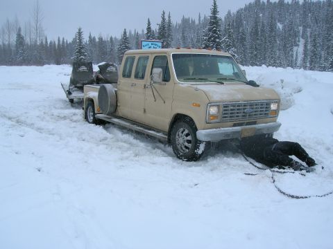 2003 Jeep TJ - A tan van and trailer loaded with snowmobiles are stuck in deep snow, with a person working underneath the front.