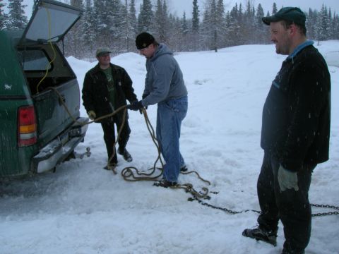 2003 Jeep TJ - Three men prepare to tow a vehicle in a snowy, wooded area, with a green pickup truck's tailgate open.