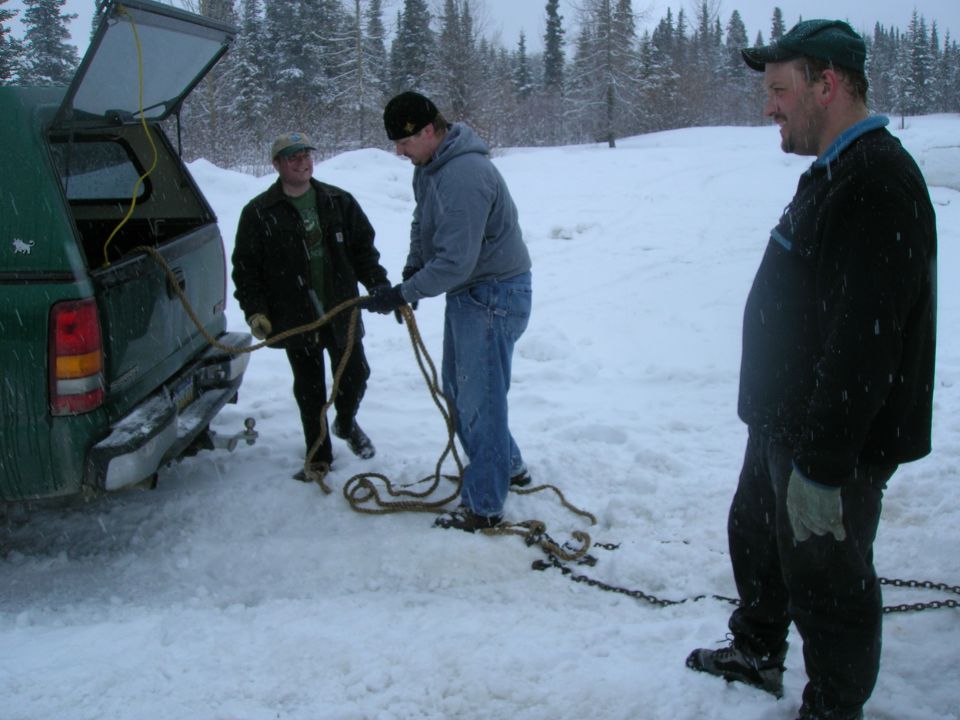 Green pickup truck rear view in snow with people handling ropes and chains