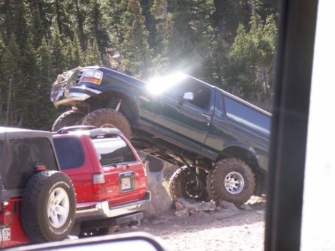 1986 Ford Bronco - A lifted green Ford Bronco navigates a rocky trail, with a red SUV behind it.