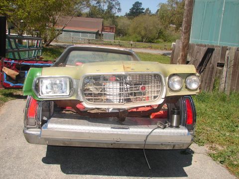 1973 Ford Ranchero - Head-on view of a faded yellow and green mid-1970s Ford Torino-style front clip with its egg-crate grille, dual round headlights on one sid…
