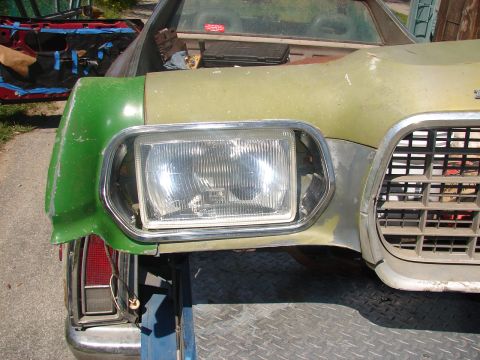 1973 Ford Ranchero - The disassembled front end of a green project car sits on a trailer, showing a single rectangular headlight, chrome trim, a mesh grille, an…