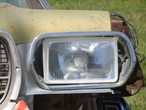 1973 Ford Ranchero - Close-up of a rectangular Lucas-marked headlamp fitted into the chrome bezel of a rusty pale-yellow front fender, with the surrounding shee…