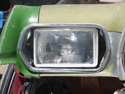 1973 Ford Ranchero - Close-up of a rectangular fluted-lens headlight in a chrome bezel set into a weathered front end painted bright green with a pale yellow-gr…