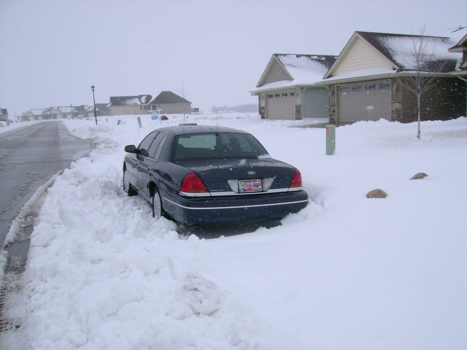 Dark blue sedan stuck in snow, rear view. License plate visible
