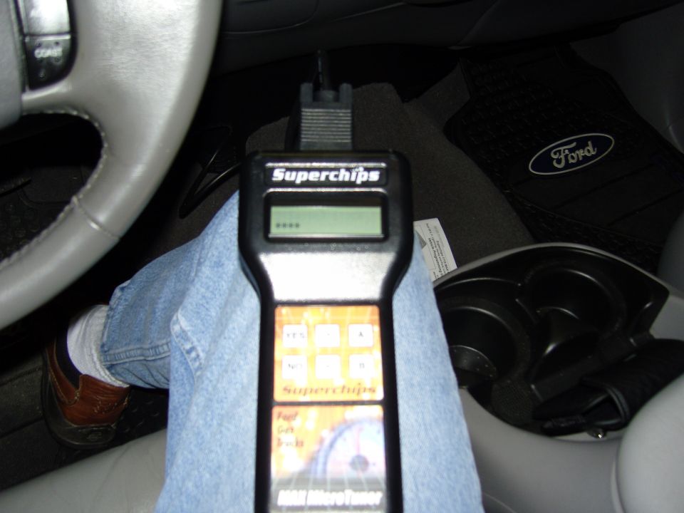 Hand holding Superchips tuner device in car. Ford floor mat visible