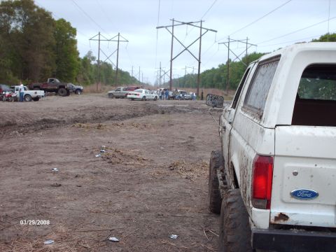 1982 Ford F-100 - White Ford Bronco parked in a muddy area with other vehicles visible in the distance.