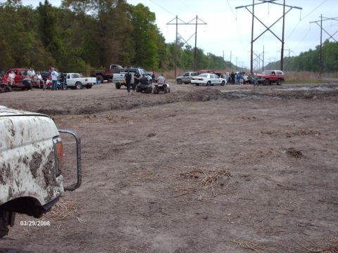1982 Ford F-100 - A group of people and vehicles are gathered in a muddy outdoor area, with power lines overhead.