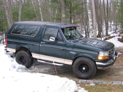 1993 Ford Bronco - Front three-quarter passenger-side view of a two-tone dark green over tan full-size Ford Bronco with a smoked windshield visor, chrome step…