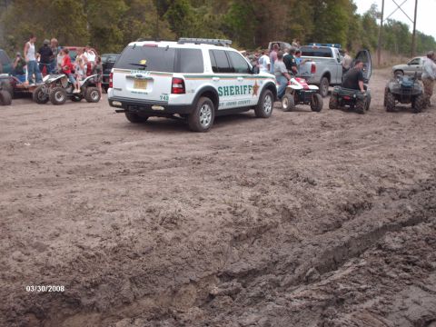 1982 Ford F-100 - A Sheriff's SUV is parked in a muddy area with several ATVs and people nearby.