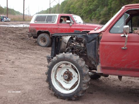 1982 Ford F-100 - A modified red pickup truck with tractor tires sits in mud next to a red SUV.