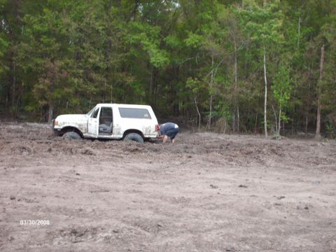 1982 Ford F-100 - A white SUV is stuck in a muddy area with trees in the background.