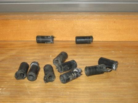 1993 Ford Bronco - Ten small black cylindrical rubber-and-metal inserts arranged loosely on a plywood workbench, each a short grommet-style bushing with a met…