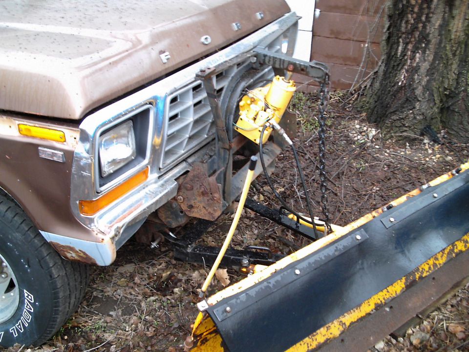 Brown Ford truck front with a yellow snow plow attachment, showing rust and wear
