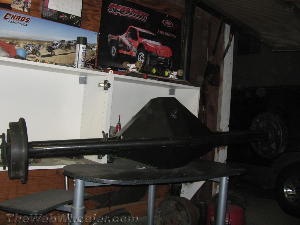 black rear axle assembly on a table, with posters on the wall behind it