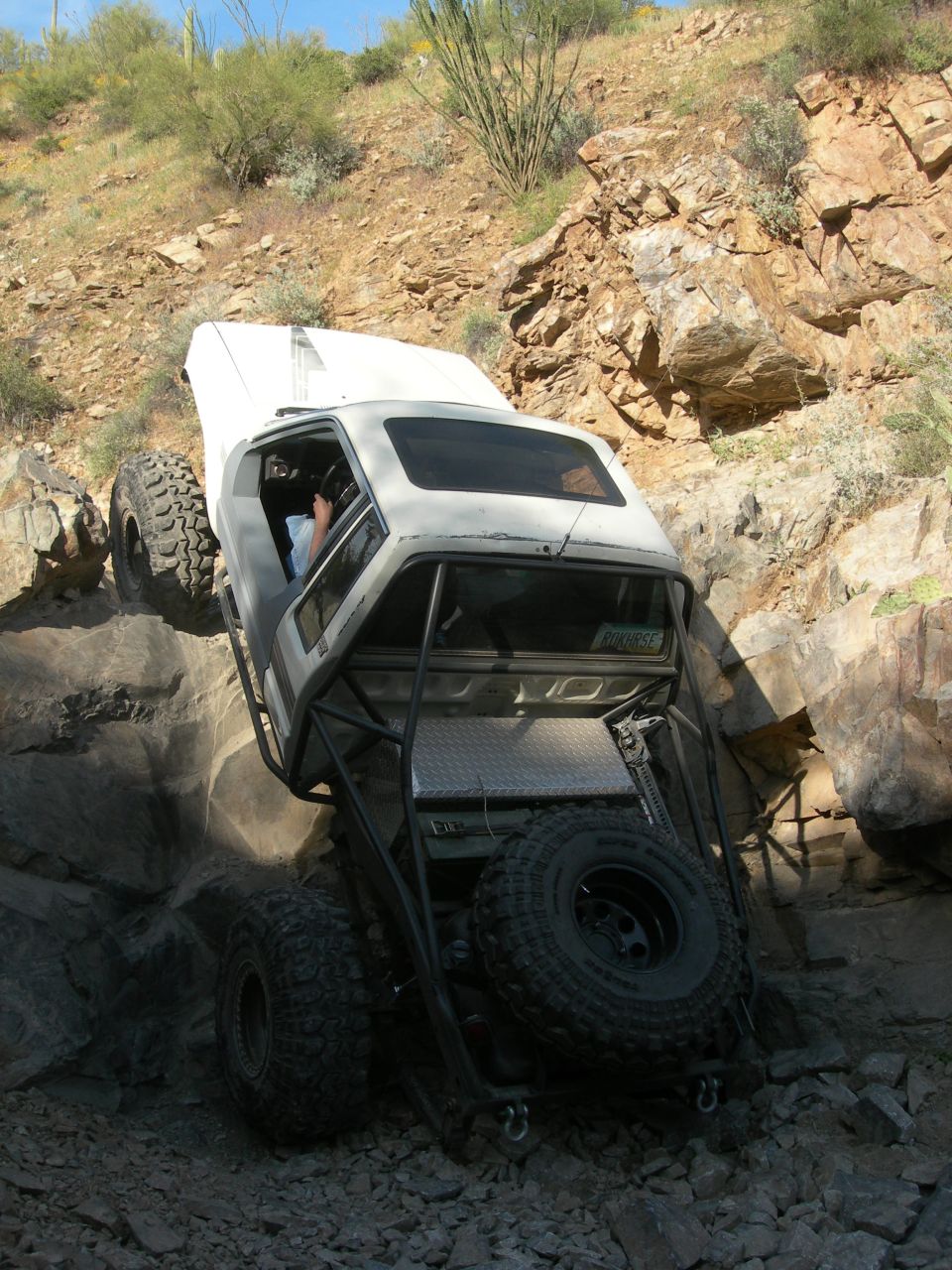 Modified pickup truck with roll cage and large tires navigating a rocky incline
