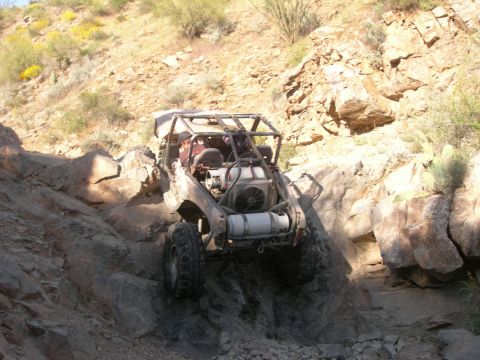 1974 Ford F-250 - A heavily modified off-road buggy navigates a steep, rocky descent in a desert environment.