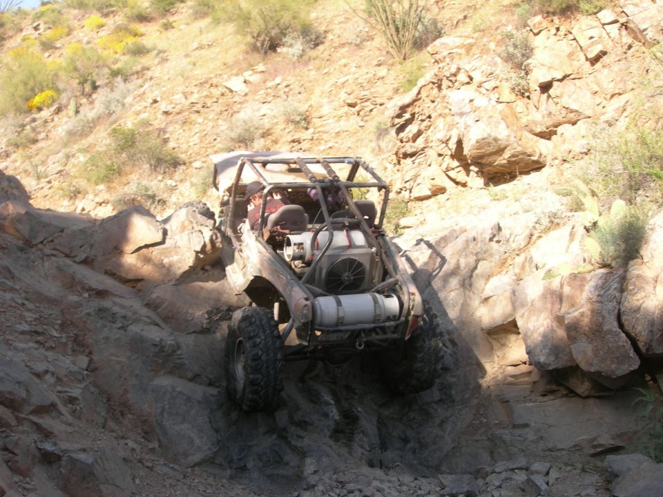 Off-road buggy with roll cage descending rocky terrain, showing exposed engine and large tires