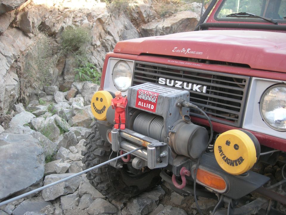 Red Suzuki Samurai on rocky terrain with a winch and smiley face lights
