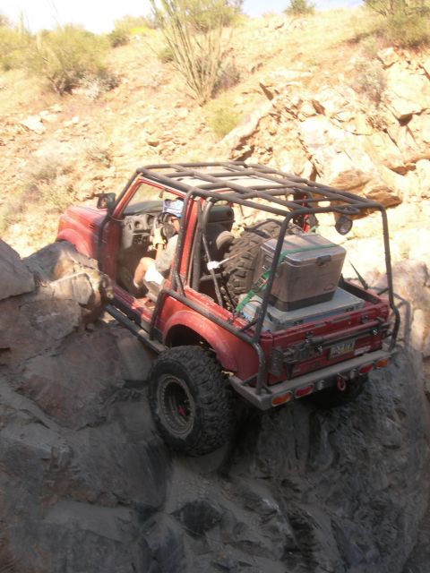 1974 Ford F-250 - A modified red off-road vehicle tackles a steep, rocky incline in a desert environment.