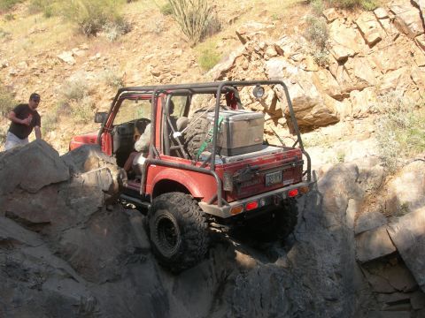 1974 Ford F-250 - A red off-road vehicle with a roll cage and spare tire navigates a challenging rocky trail.