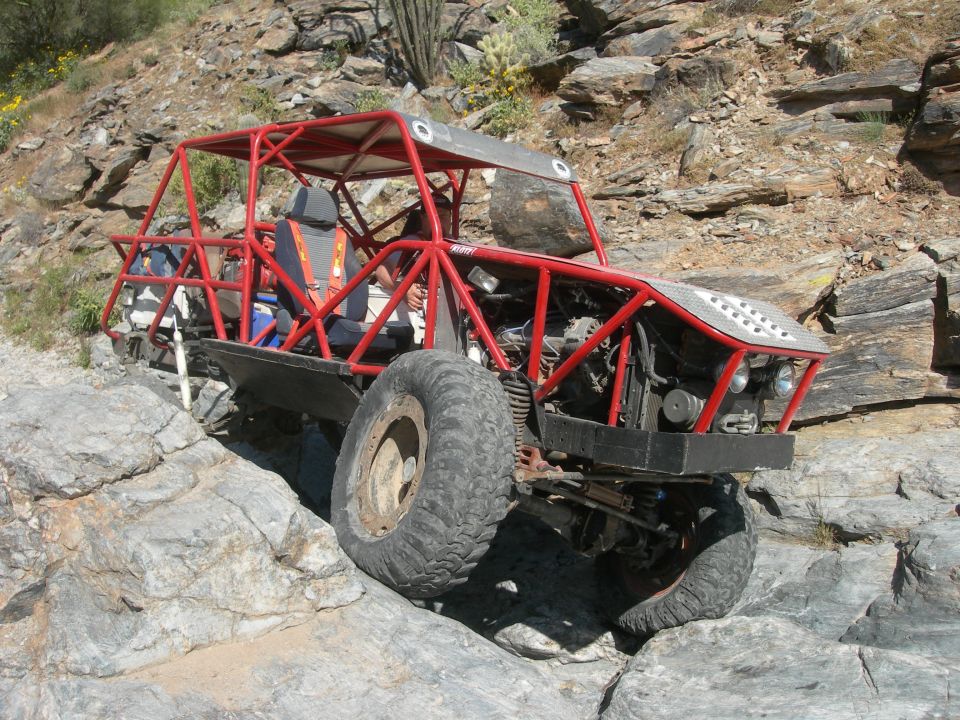 Red tube-frame buggy with large tires climbing over rocks in a desert canyon