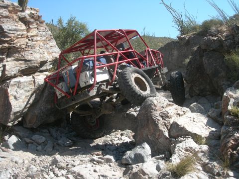 1974 Ford F-250 - A heavily modified off-road buggy tackles a challenging rocky trail under a clear blue sky.