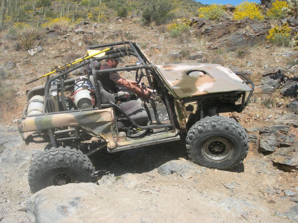 Custom off-road buggy with camouflage paint, large tires, and roll cage on rocky terrain