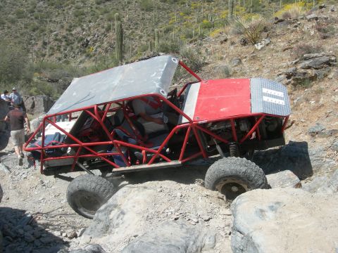 1974 Ford F-250 - A heavily modified off-road buggy traverses a challenging rocky landscape under a bright sun.