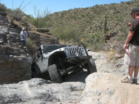 1974 Ford F-250 - Jeep Wrangler tackling a difficult off-road obstacle in a desert landscape.