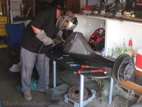 1968 Ford Mustang - A person welds a car's rear axle assembly in a cluttered garage environment.
