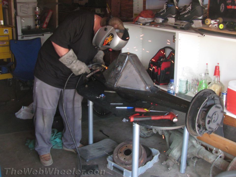 Car rear axle assembly with brake drums, being welded by a person in a garage