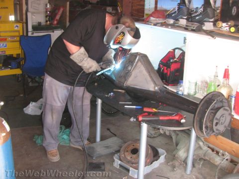 1968 Ford Mustang - A person welds a rear axle assembly in a cluttered garage environment.