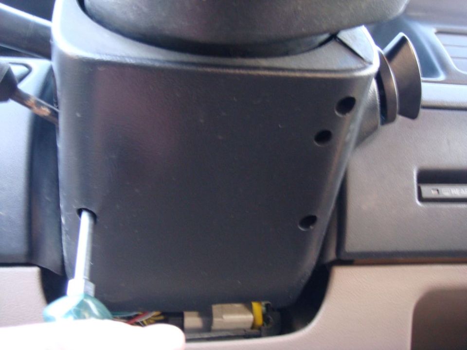 Close-up of a black plastic steering column cover with a screwdriver inserted