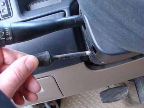 1996 Ford Bronco - A close-up view of a hand adjusting a screw on the steering column, near the turn signal stalk.