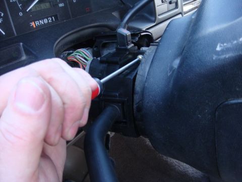 1996 Ford Bronco - A hand uses a screwdriver to work on the steering column interior, with the gear indicator visible on the dashboard.