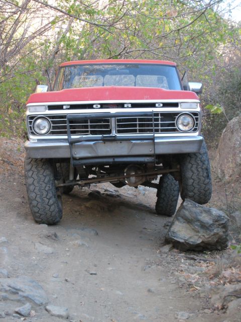 1974 Ford F-250 - This red Ford pickup truck is navigating a rough, rocky terrain with its front wheels angled.