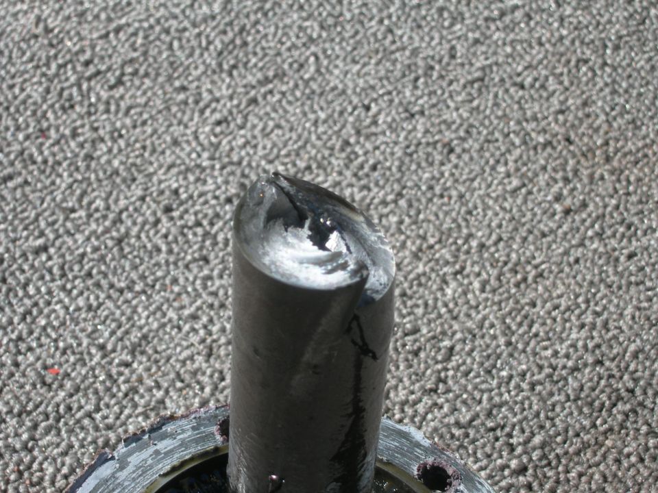 Broken metal shaft with jagged edges, resting on a grey carpet-like surface