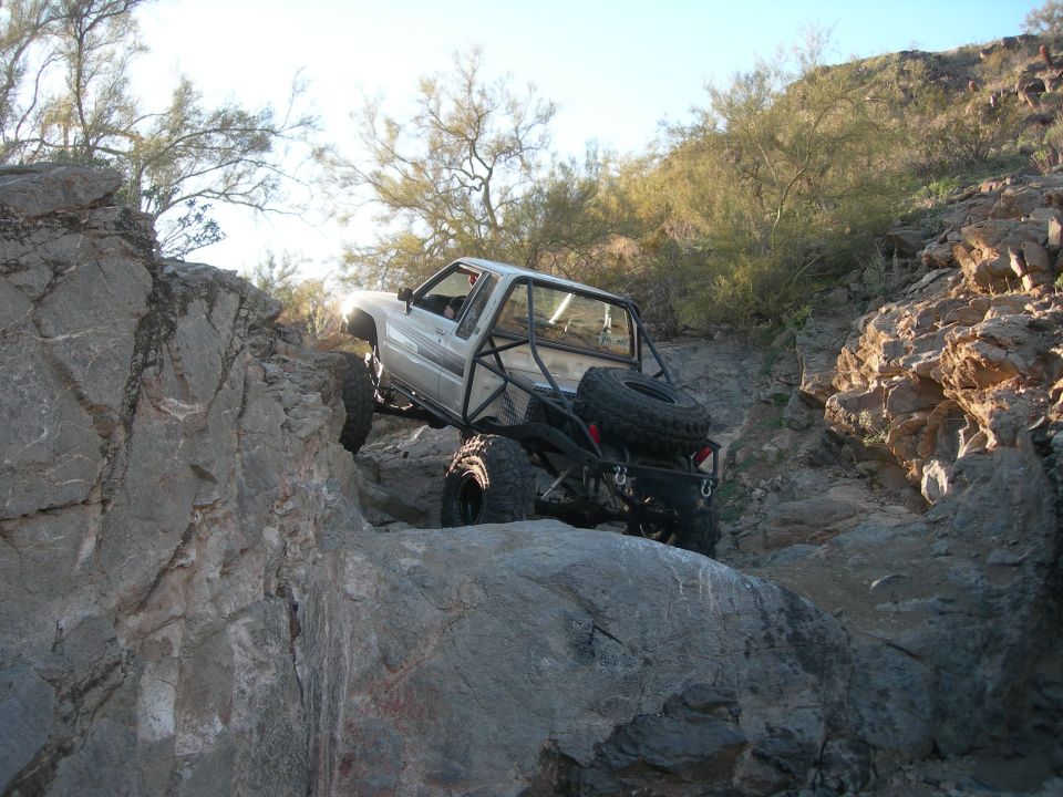 Silver pickup truck with roll cage climbing rocks